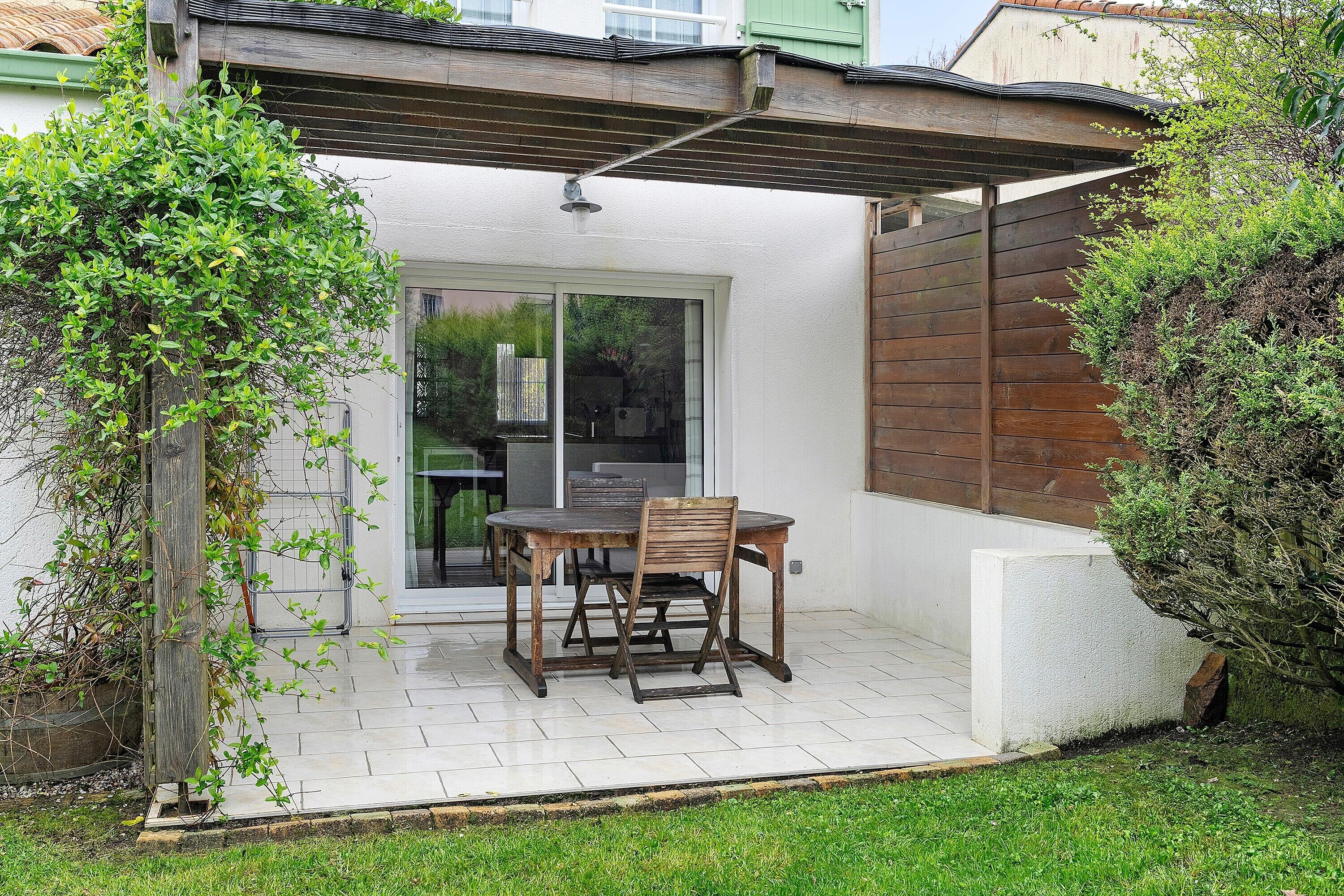 Une terrasse avec une table et des chaises, une pergola et une vue sur l’intérieur.