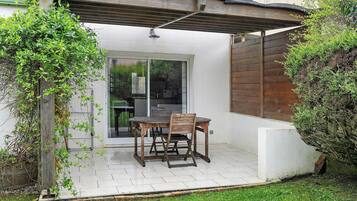 Une terrasse avec une table et des chaises, une pergola et une vue sur l’intérieur.