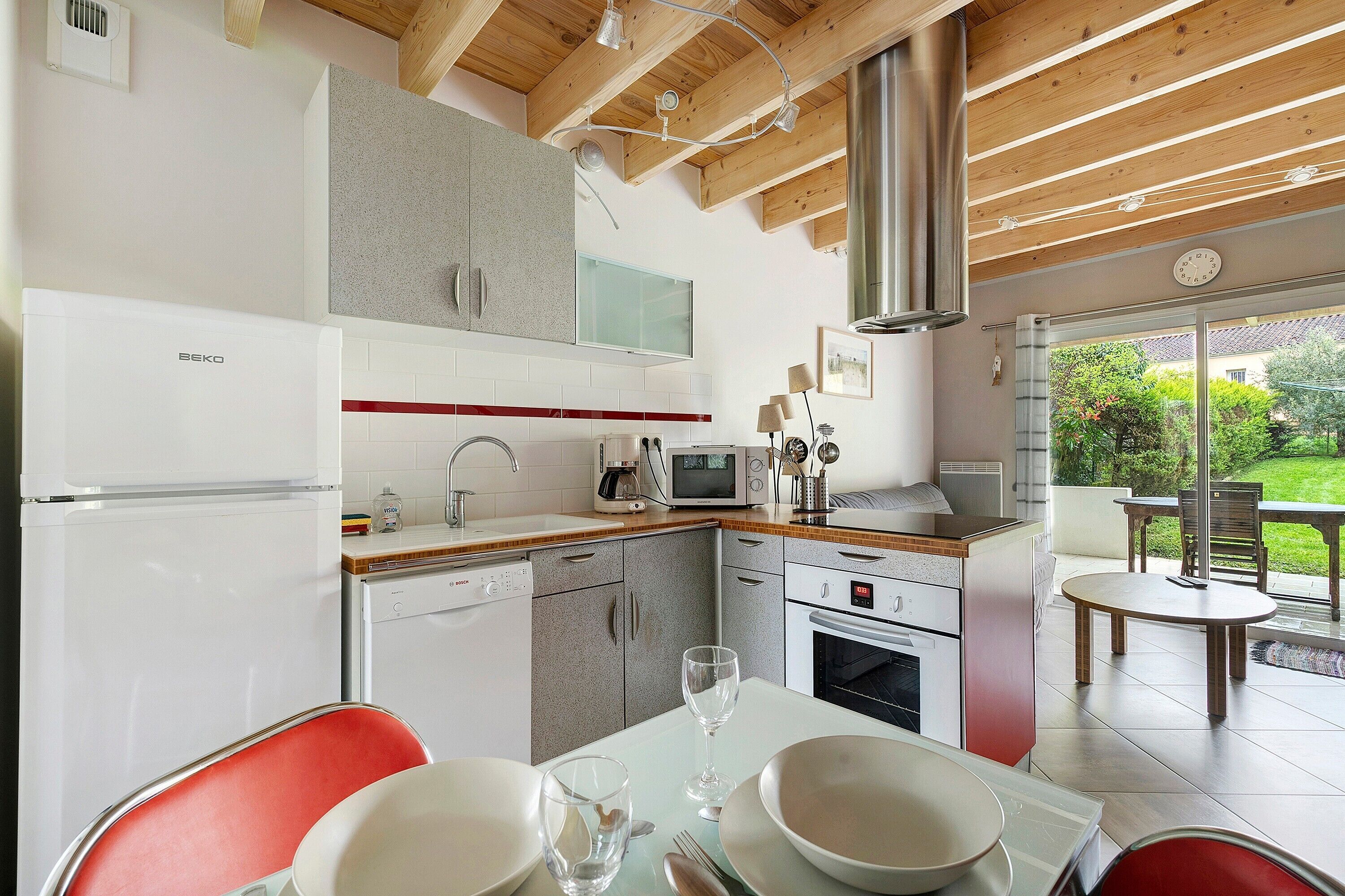A modern kitchen with a dining area, wooden ceiling beams, and a view of the garden.
