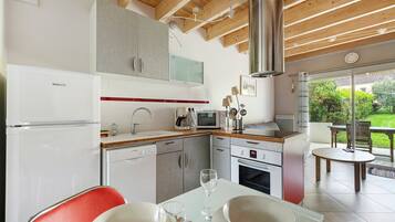 A modern kitchen with a dining area, wooden ceiling beams, and a view of the garden.