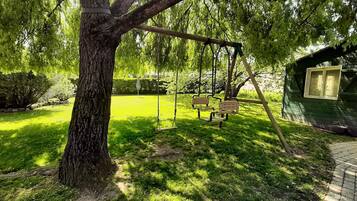 Ein Baum mit einer Schaukel, ein grünes Gebäude und eine gepflasterte Fläche.