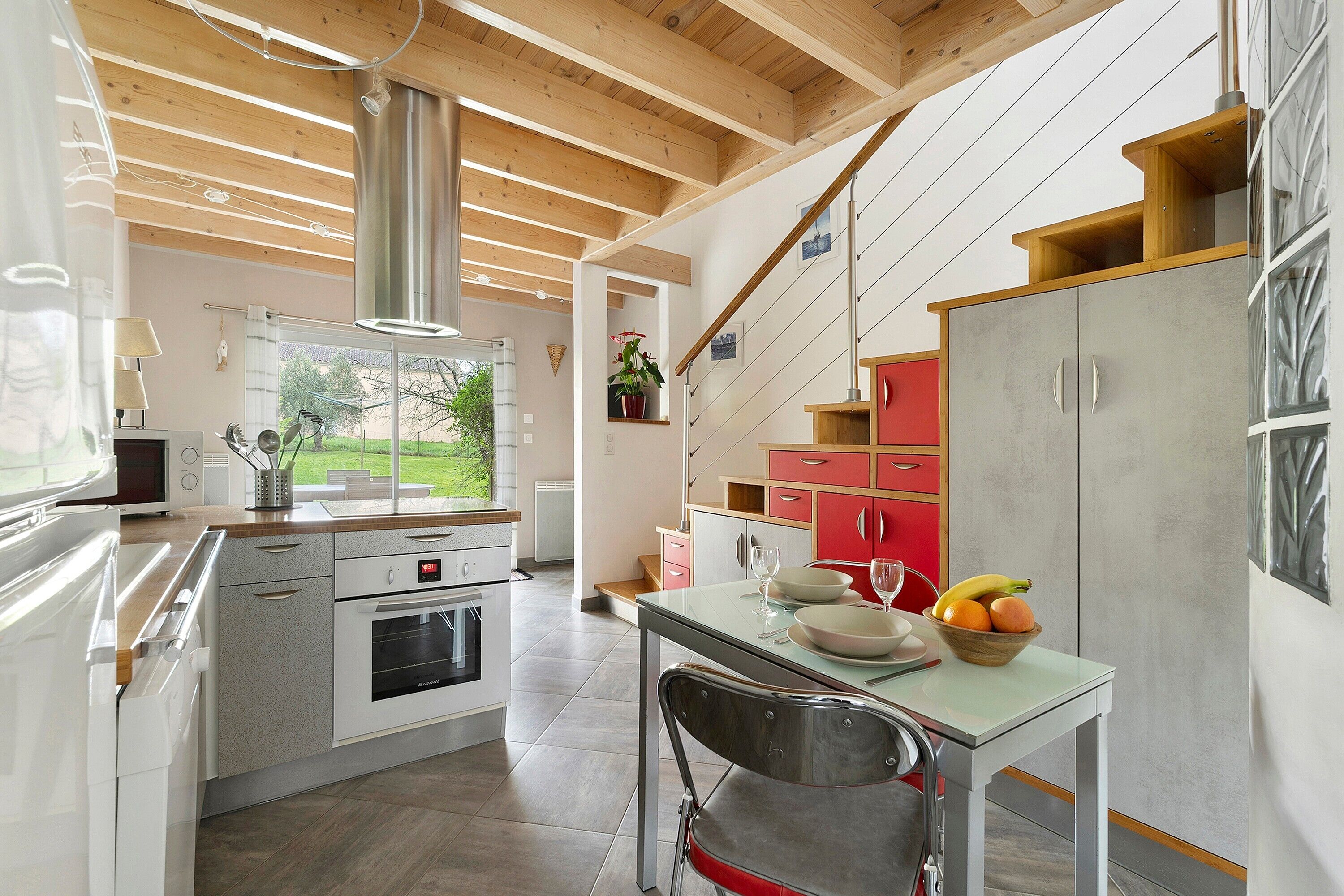 A modern kitchen with wooden beams, stainless steel appliances, and a dining area with a table set for two.