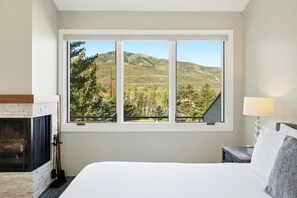 Ein Schlafzimmer mit großem Fenster, Kamin und Nachttisch mit Lampe.
