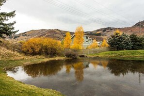 A house with a pond in front, surrounded by autumn-colored trees and hills. - Snowcap Lodge | Sauna, Hot Tub & Mountain Fun (Park City)