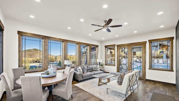 A spacious living room with a dining area, large windows, and a ceiling fan. - Greg's Canyons Home Walk Ski Lift Private Hot Tub (Park City)