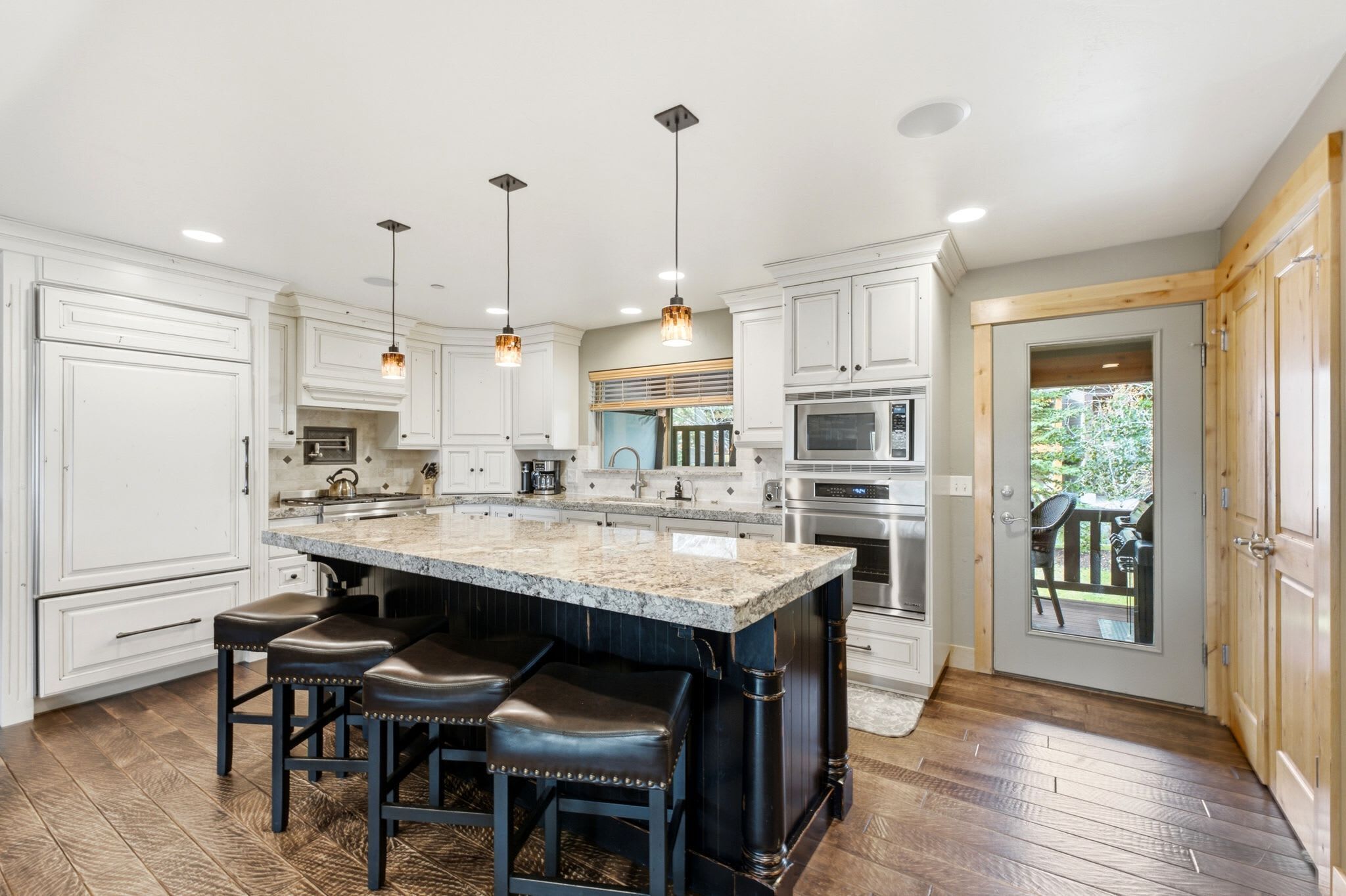 A modern kitchen with white cabinetry, a large island with bar stools, stainless steel appliances, and pendant lighting.