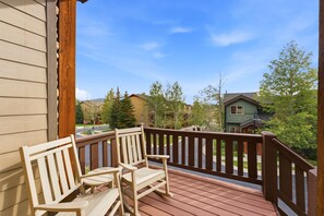 Um deck de madeira com duas cadeiras e guarda-corpo, com vista para uma área residencial com casas e árvores.
