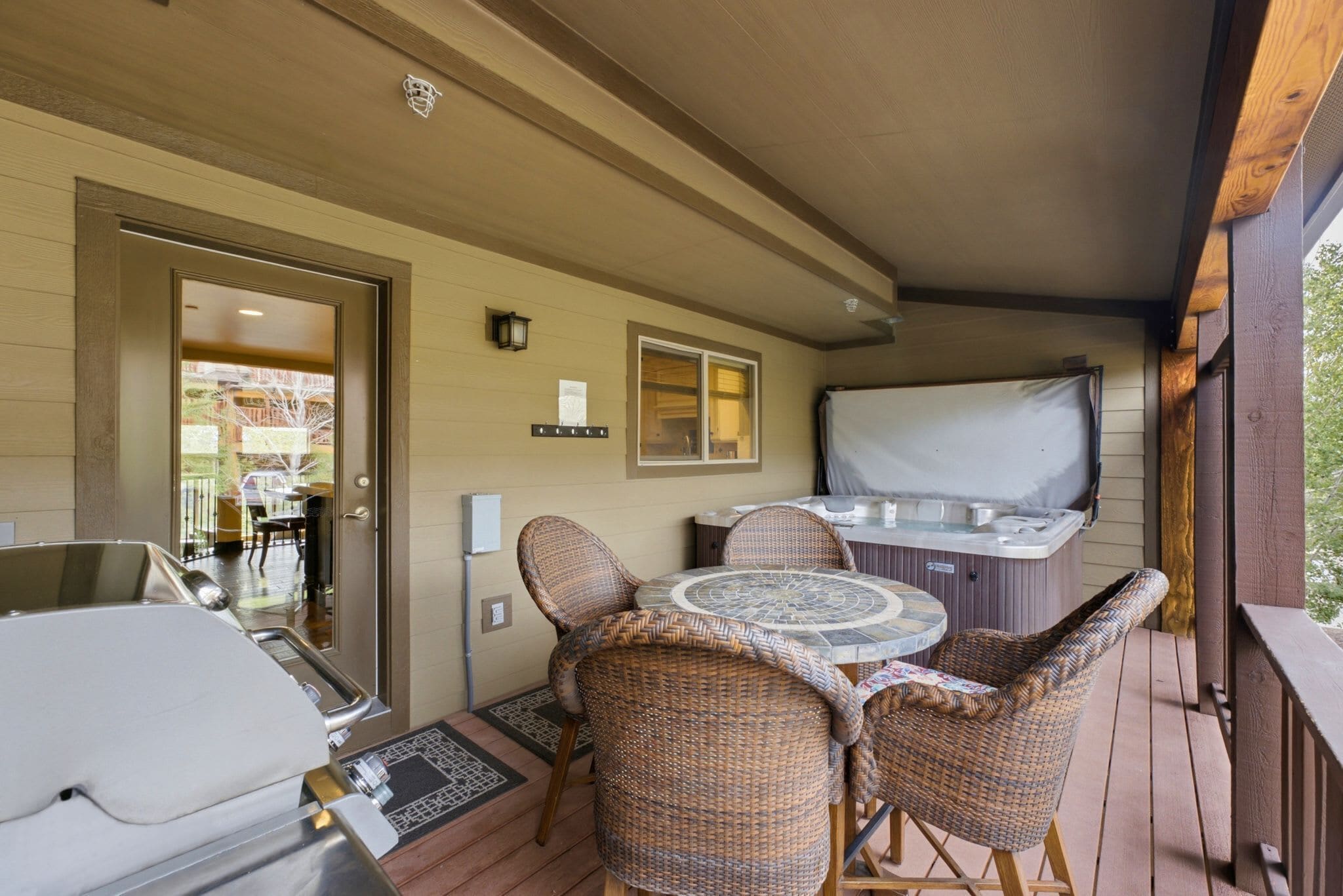 A covered outdoor area with wicker furniture, a hot tub, and a grill.