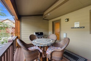 A covered outdoor patio with a round table and wicker chairs, a grill, and a door to the right. - Family Friendly Townhouse with Private Hot Tub (Park City)
