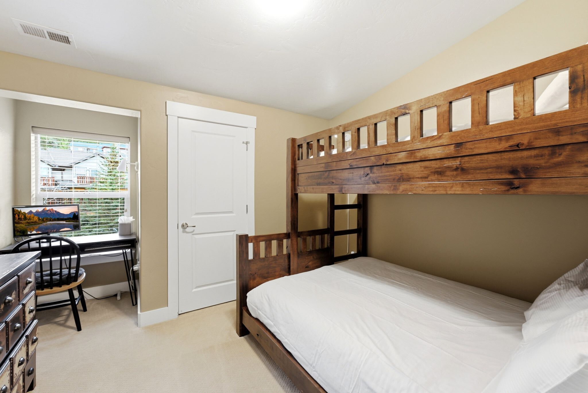 Una cama litera con cabecera de madera, un escritorio con silla y una ventana con persianas.