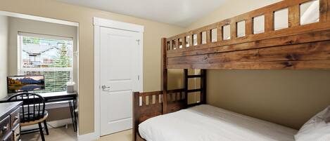Una cama litera con cabecera de madera, un escritorio con silla y una ventana con persianas.