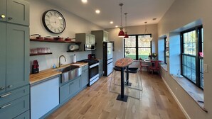 A modern kitchen with light blue cabinets, a wooden countertop, and a large wall clock. - New renovation retro-Modern 1960s Service Station • Fireplace • 100″ TV•garage (Nunica)