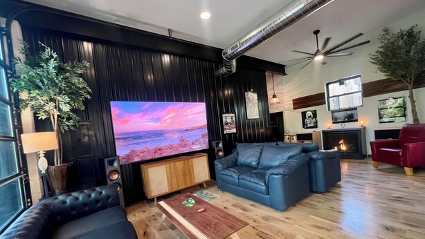 A modern living room with a large flat-screen TV, leather sofas, a wooden coffee table, and a fireplace. - New renovation retro-Modern 1960s Service Station • Fireplace • 100″ TV•garage (Nunica)