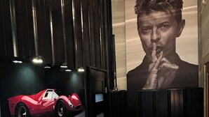 A room with a television mounted on a dark wall, a wooden bench, and a poster of a man with a hand gesture. - New renovation retro-Modern 1960s Service Station • Fireplace • 100″ TV•garage (Nunica)