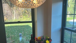 A dining area with a wooden table, red chairs, a vase with flowers, and a bottle of wine. - New renovation retro-Modern 1960s Service Station • Fireplace • 100″ TV•garage (Nunica)