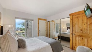 Ein Schlafzimmer mit einem Bett, einer Holztür und Blick ins Freie.