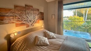 A bedroom with a bed, a painting of trees, a hot tub, and a balcony with a view of trees. - L'ESCALE COTE BLEUE VILLA & Spa 4étoiles (Sausset-les-Pins)