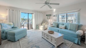Un salón espacioso con un ventanal grande, un ventilador de techo y vistas a un edificio con la leyenda 'FORT MYERS'.