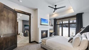 Un dormitorio con una cama grande, chimenea, ventilador de techo y vistas a un paisaje nevado.