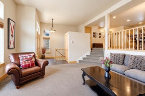 A spacious living area with a leather armchair, a sofa, a coffee table, and a staircase leading to an upper floor. - Bears Lair | Private Hot Tub & Mountain Views (Park City)