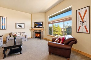 A living room with a fireplace, a sofa, a coffee table, and artwork on the walls. - Bears Lair | Private Hot Tub & Mountain Views (Park City)