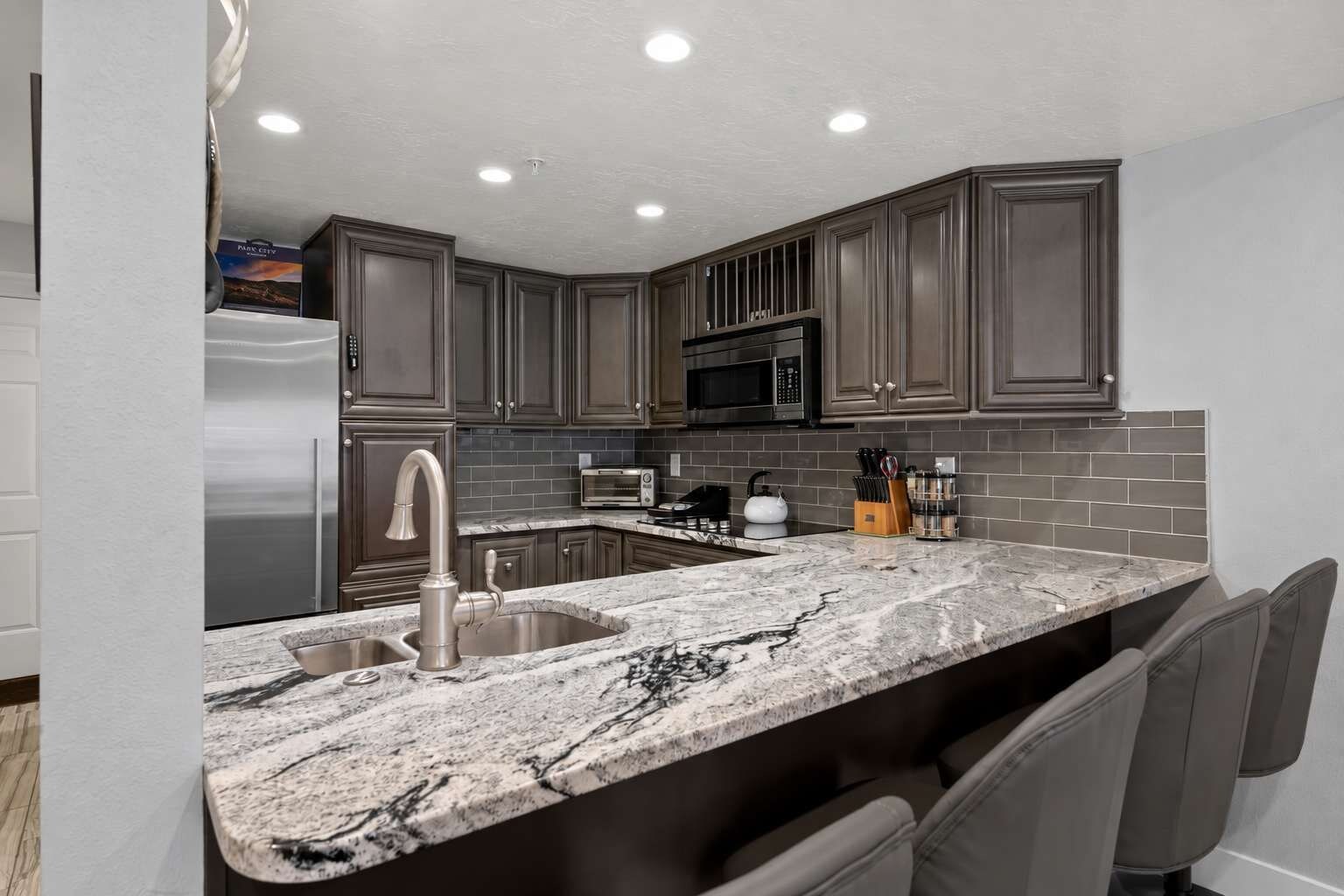 A modern kitchen with dark wood cabinets, a stainless steel refrigerator, a microwave, and a granite countertop.