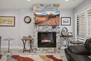 Un salon doté d’une cheminée en pierre, d’un téléviseur à écran plat placé au-dessus et d’un tableau représentant un paysage, encadré, accroché au mur.
