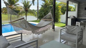 Ein modernes Zimmer mit einer Hängematte, einem Pool und Blick auf Palmen.