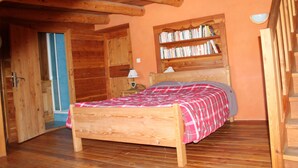 Un dormitorio con estructura de madera, una cama, una estantería y una escalera de madera.