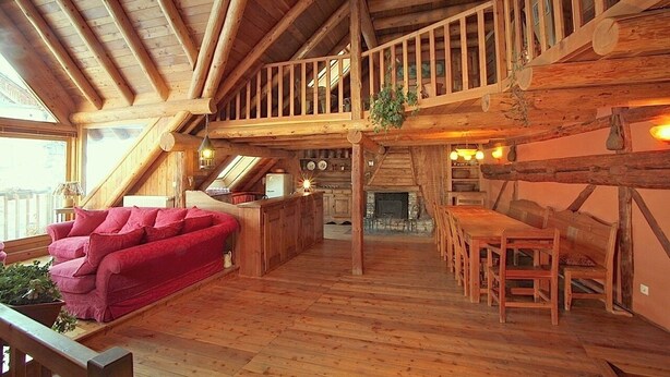 Amplio espacio tipo loft con techo de madera, un sofá rojo, una mesa de comedor con sillas y una chimenea.