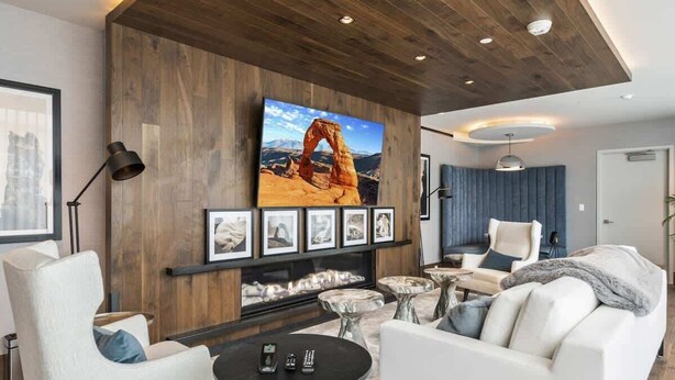 A modern living room with a large TV mounted on a wooden wall, a fireplace, and comfortable seating. - New! Lux Studio Lake Views | Trails & Adventure | Free shuttle to Gondola (Park City)