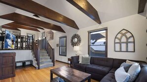 A spacious living room with a dark brown sofa, a wooden coffee table, and a staircase with wooden beams. - Charming Chalet in Old Town & Pet Friendly (Park City)