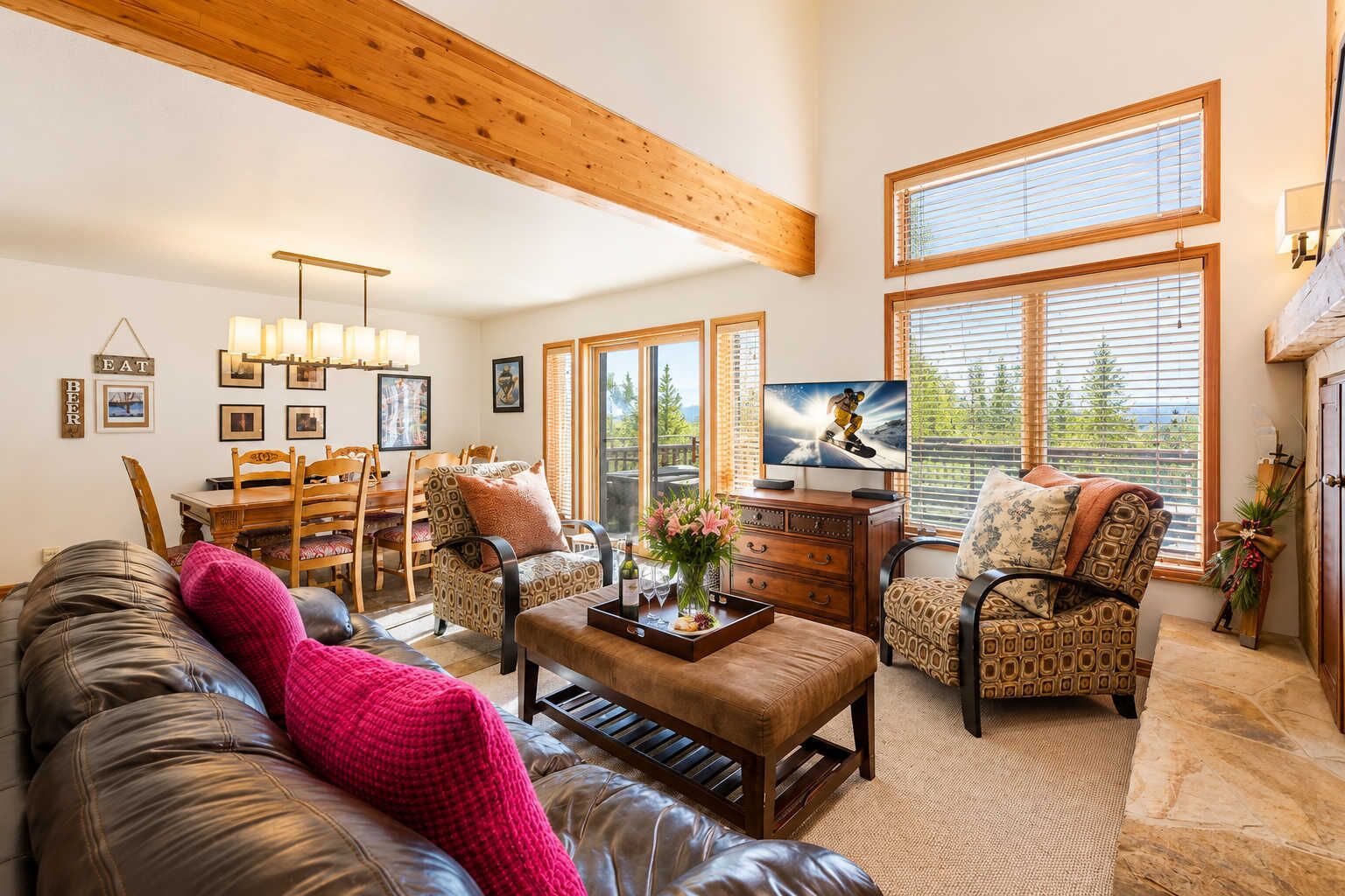 A spacious living room with a wooden ceiling, large windows, a television, and a dining area.