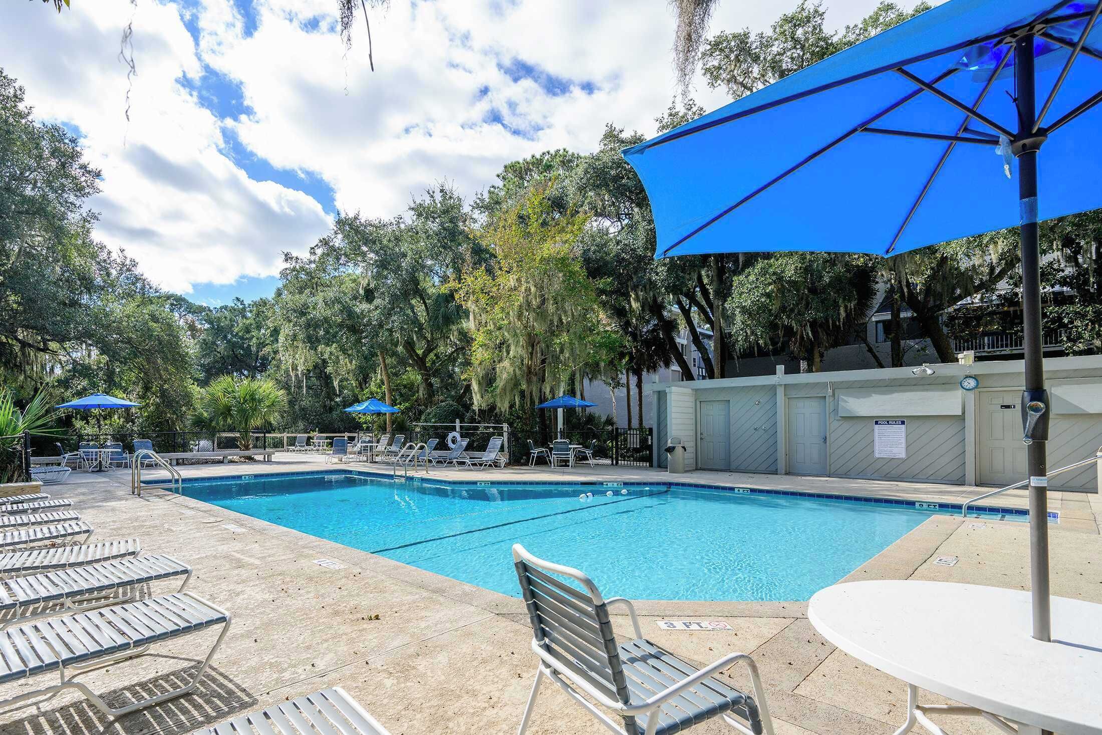 A swimming pool with lounge chairs and umbrellas, surrounded by trees.