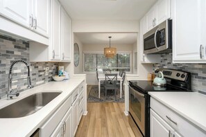 Una cocina con armarios blancos, un lavamanos de acero inoxidable, un microondas y una estufa.