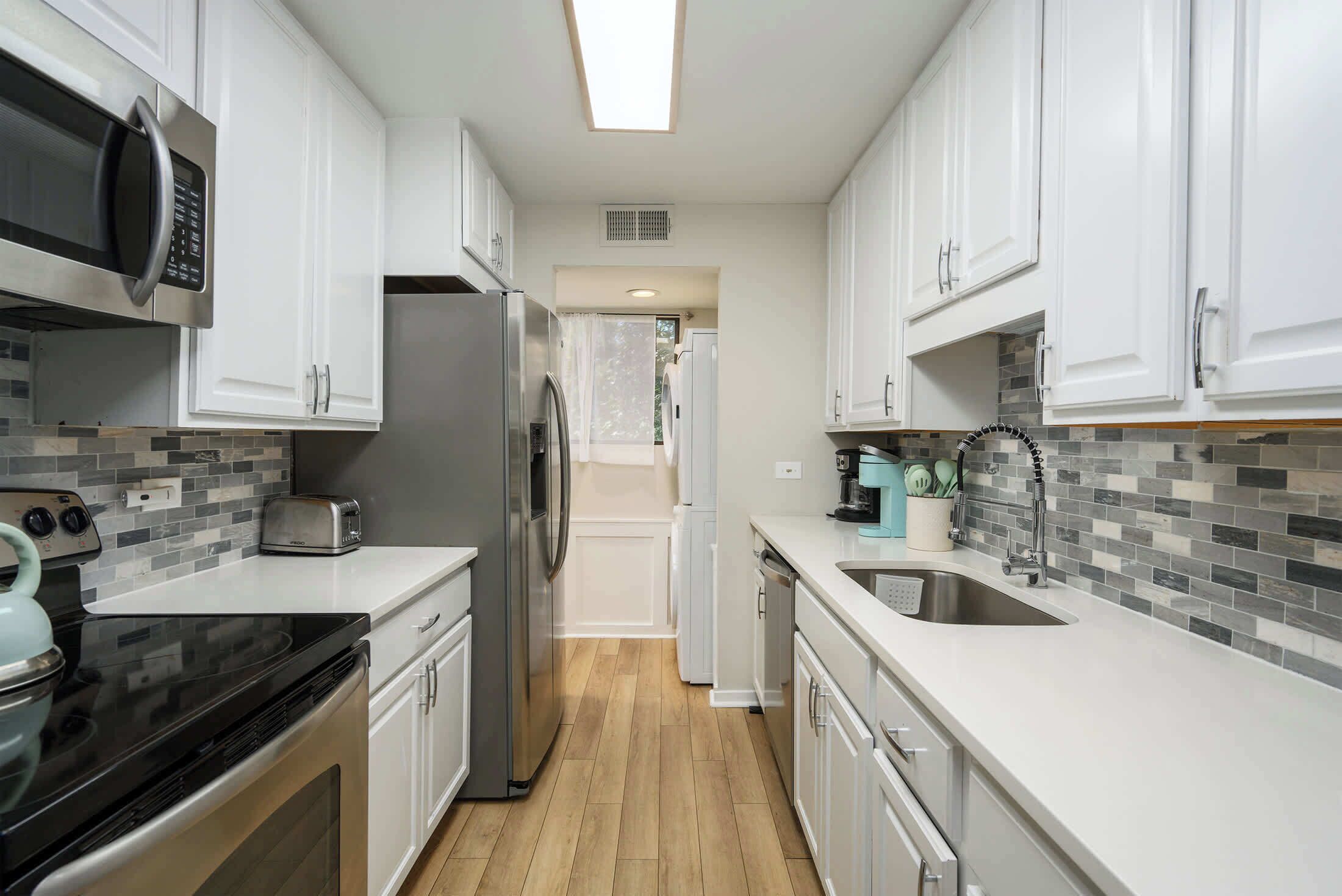 A modern kitchen with white cabinets, a stainless steel refrigerator, a microwave, and a dishwasher.