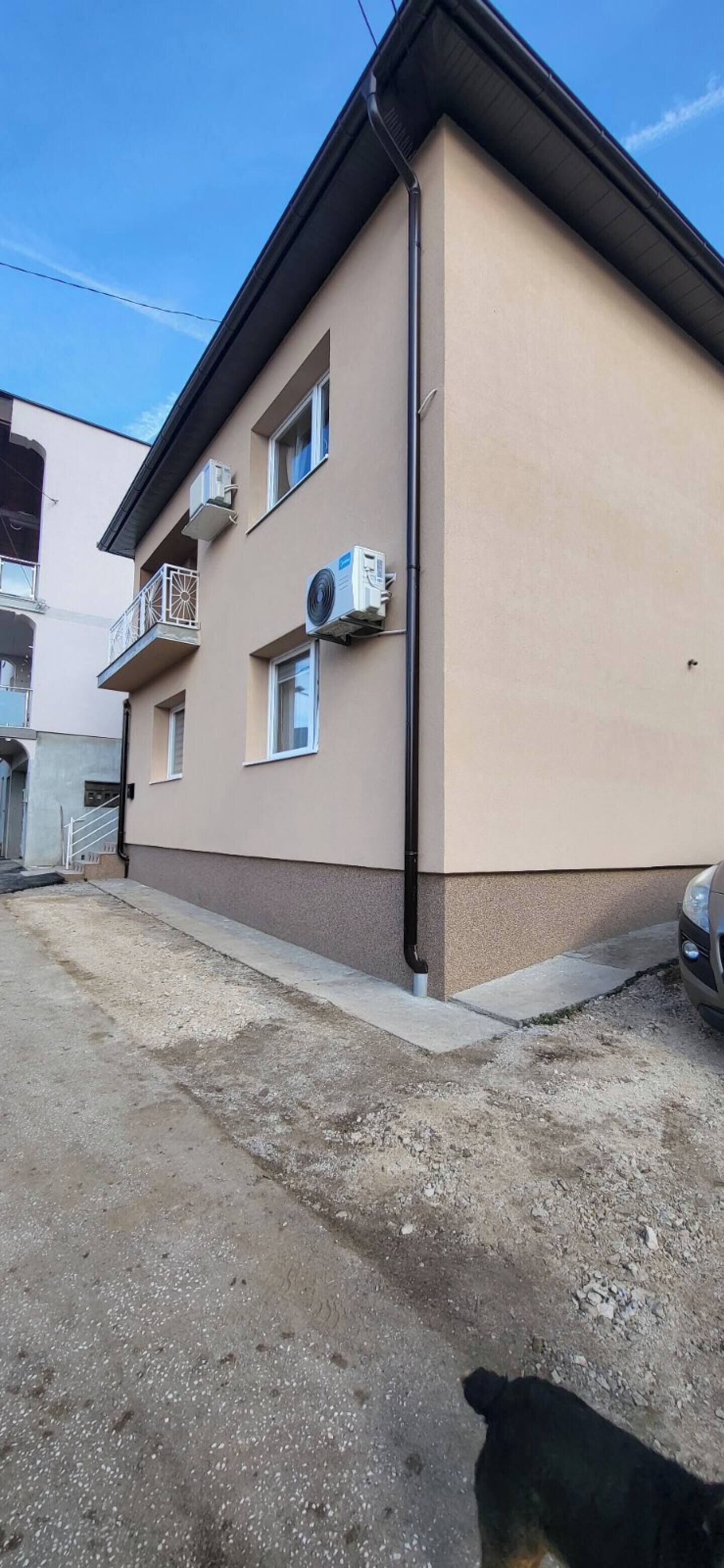 Un edificio de dos pisos con unidades de aire acondicionado, un balcón y un coche estacionado adelante.