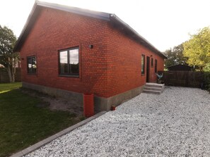 A red brick house with a gravel driveway and a wooden fence in the background. - Cozy 4-bedroom Holiday Home in Vesterø Havn, Denmark (Læsø)