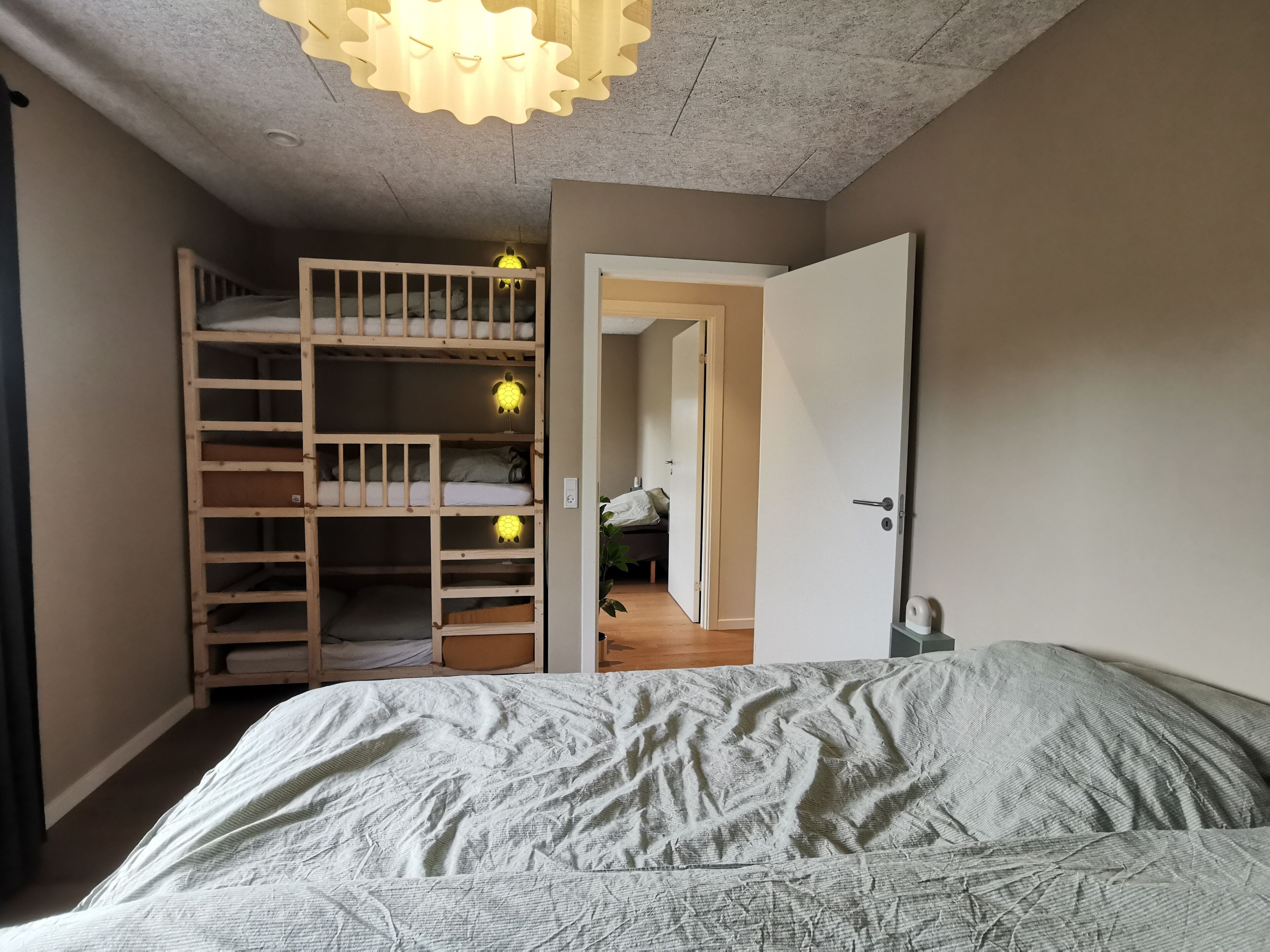 A bedroom with a bunk bed, a door leading to another room, and a ceiling light fixture.