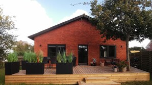 Une maison en briques rouges avec une terrasse en bois, des meubles d’extérieur et des plantes en pot.