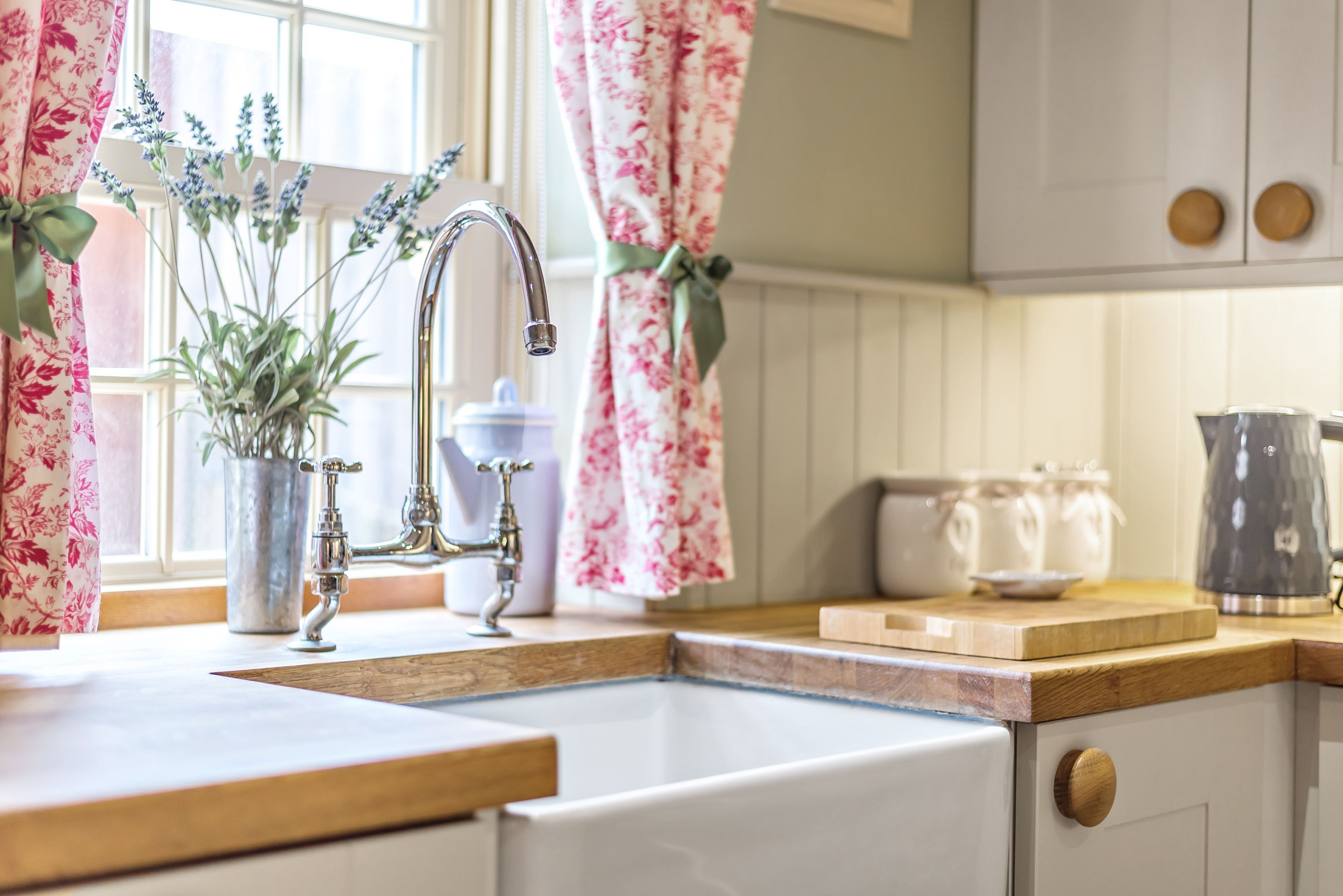 A kitchen with a wooden countertop, a sink, and a window with floral curtains.