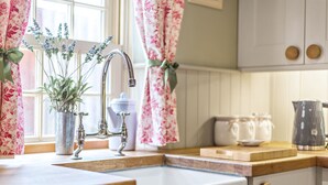 Een keuken met een houten aanrecht, een spoelbak en een raam met bloemen gordijnen.