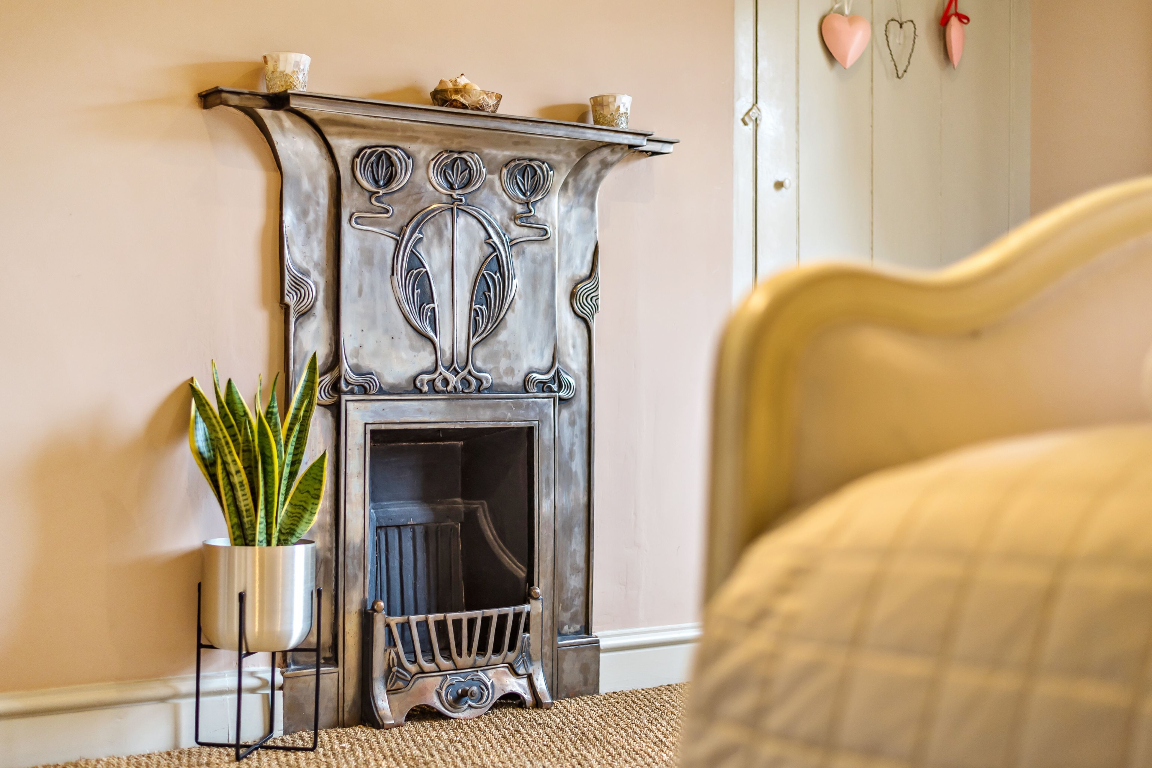 A room with a vintage fireplace, a potted plant, and a bed with a patterned bedspread.