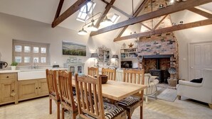A spacious kitchen with wooden beams, a brick fireplace, and a dining area with wooden chairs. - The Foundry - sleeps 6 guests  in 3 bedrooms (Burnham Market)