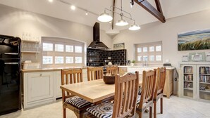 A spacious kitchen with a wooden dining table, chairs, and a built-in bookshelf. - The Foundry - sleeps 6 guests  in 3 bedrooms (Burnham Market)