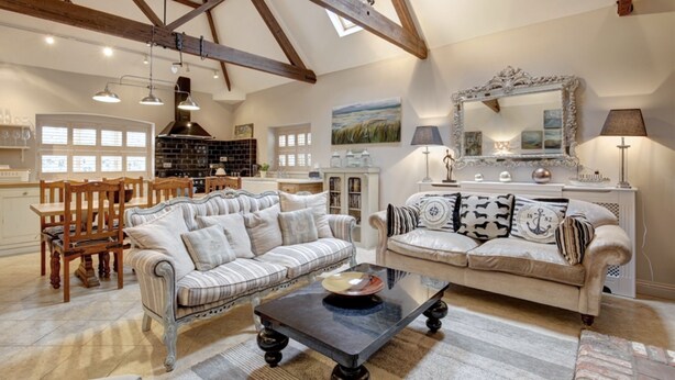A spacious living room with high ceilings and exposed beams, featuring two sofas, a coffee table, and a fireplace. - The Foundry - sleeps 6 guests  in 3 bedrooms (Burnham Market)