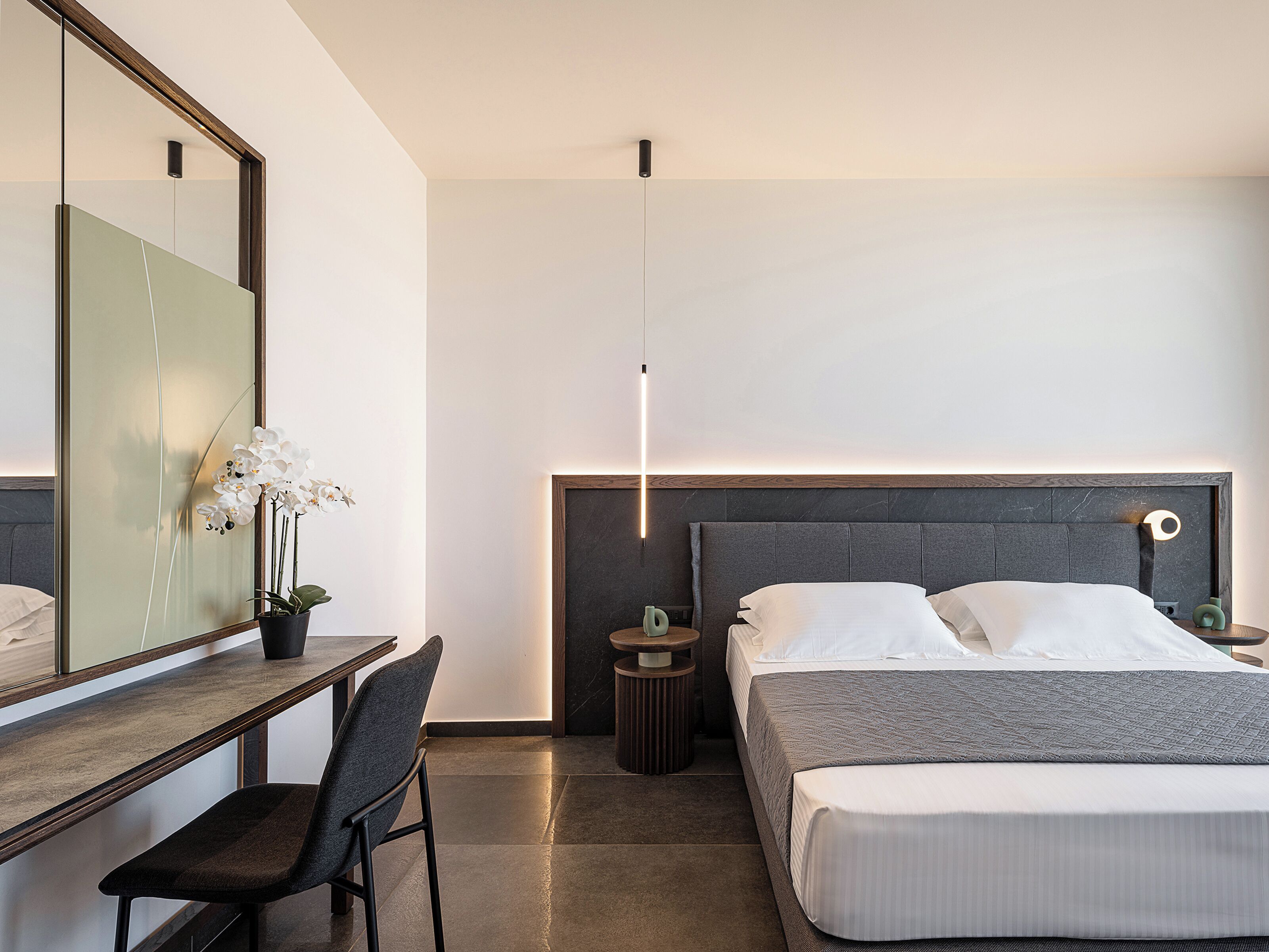 Un dormitorio moderno con cama, mesita de noche, silla y un espejo grande.