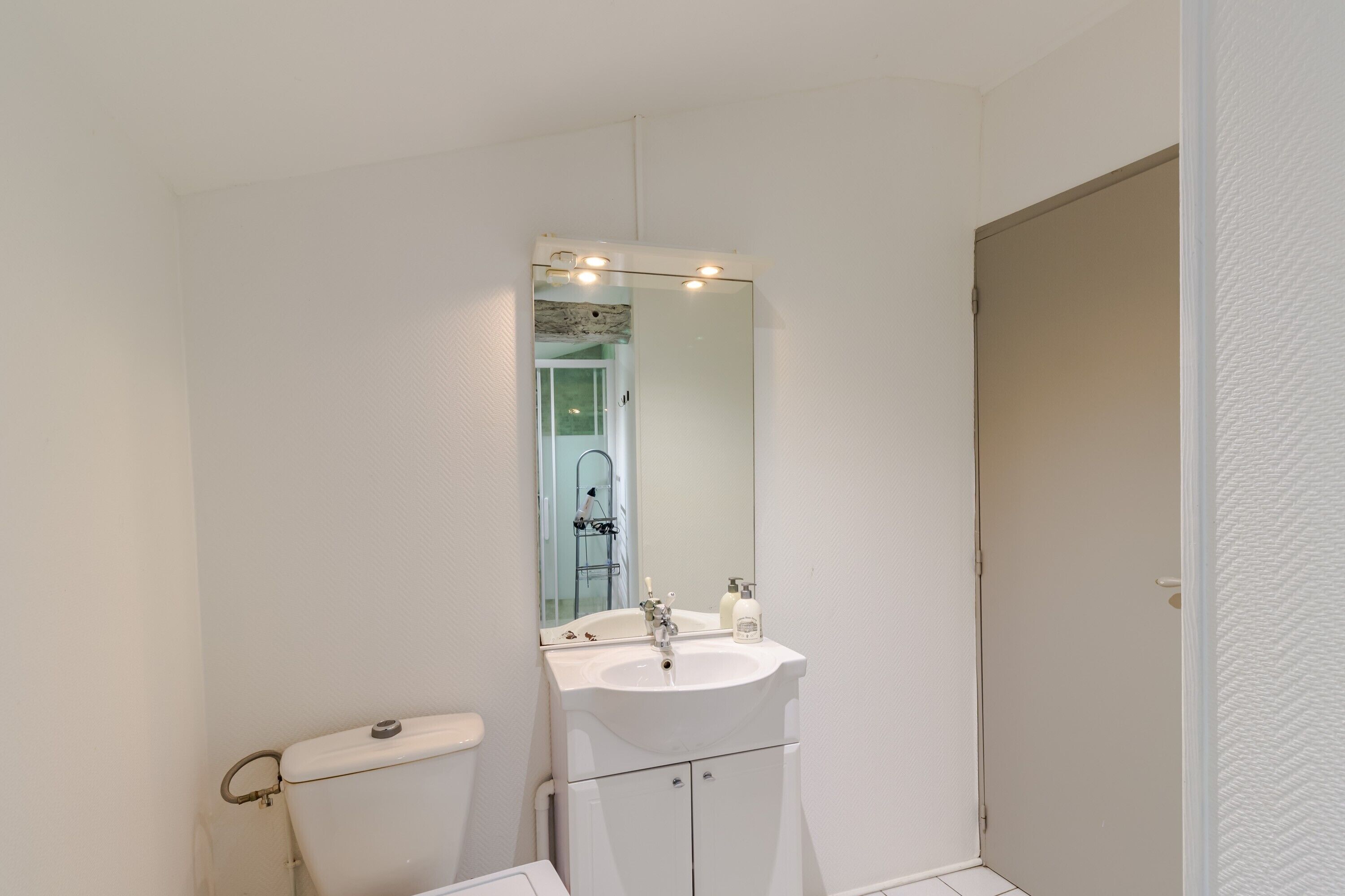 A bathroom with a white sink, mirror, and toilet.