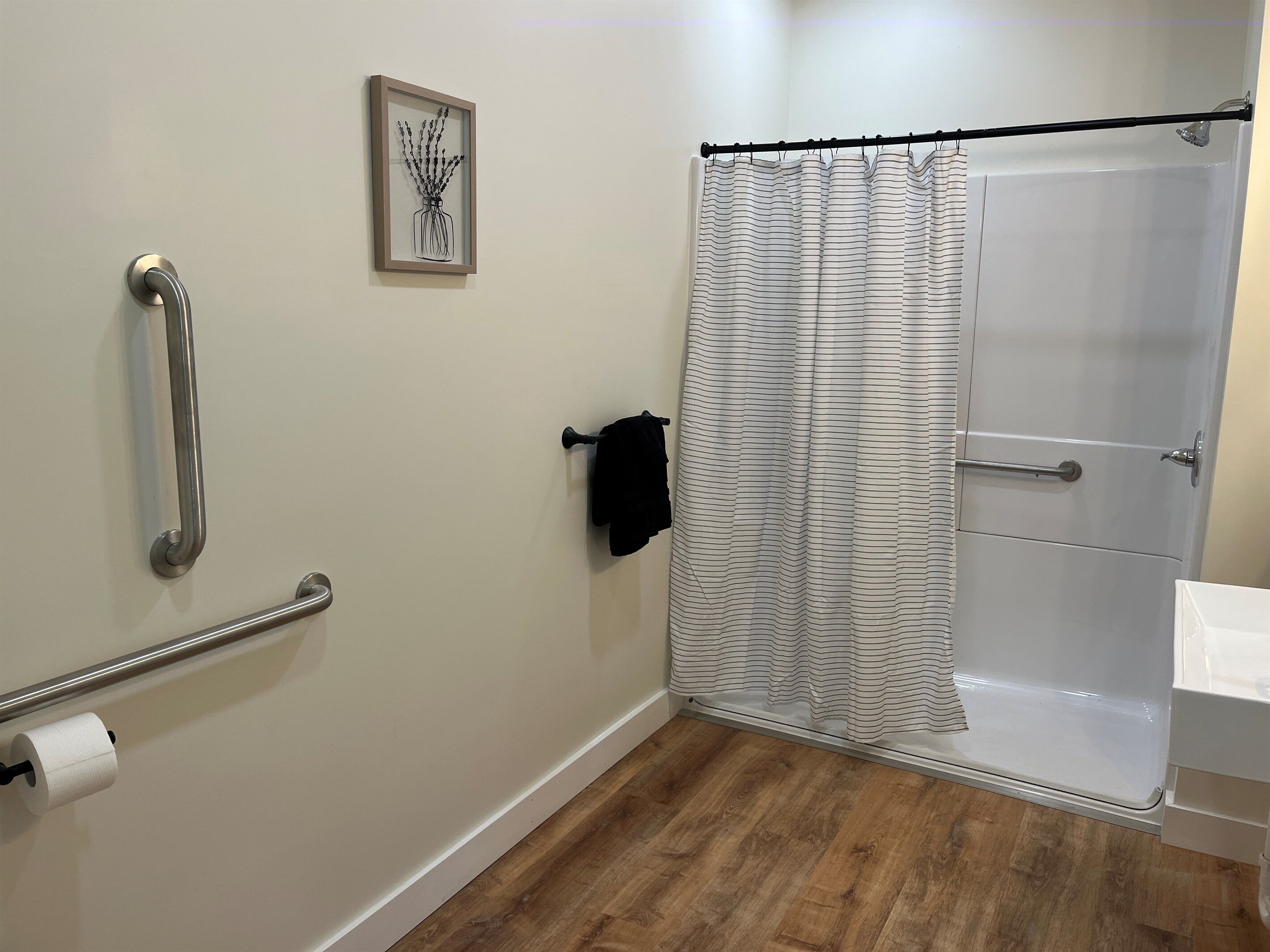 A bathroom with a shower, a toilet paper holder, a towel rack, and a framed picture on the wall.