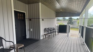 Un espacio al aire libre cubierto con piso de madera, sillas de metal y una puerta que da a un ambiente interior.